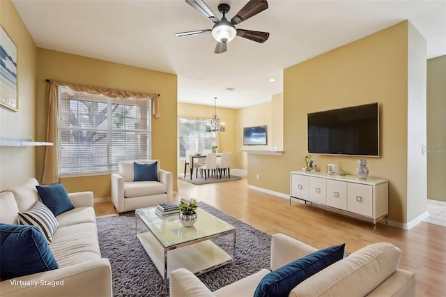 living room with ceiling fan with notable chandelier and light hardwood / wood-style flooring