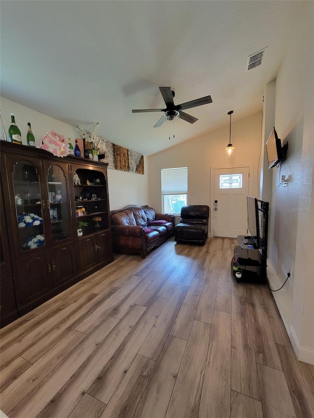 living room featuring vaulted ceiling, light wood-type flooring, visible vents, and a ceiling fan