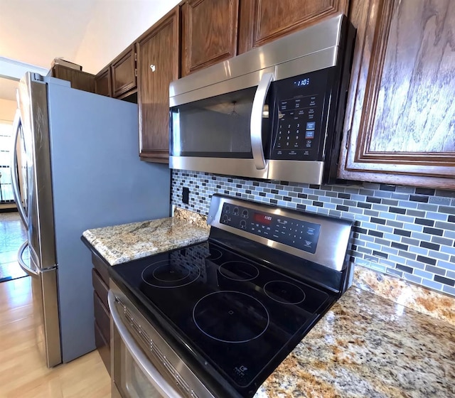 kitchen featuring stainless steel appliances, tasteful backsplash, dark brown cabinets, and light stone counters