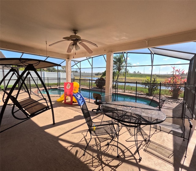 view of patio / terrace with ceiling fan, a water view, glass enclosure, a hot tub, and a playground