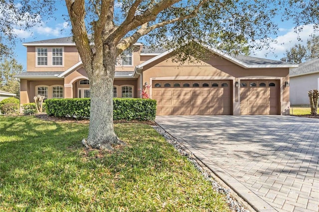 view of front facade with a garage, decorative driveway, a front yard, and stucco siding