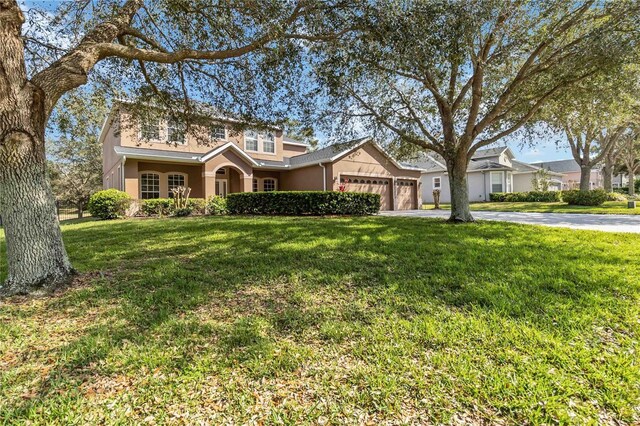 traditional-style house featuring a garage, driveway, a front lawn, and stucco siding