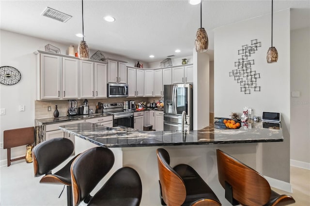 kitchen featuring visible vents, appliances with stainless steel finishes, decorative light fixtures, a peninsula, and a kitchen bar