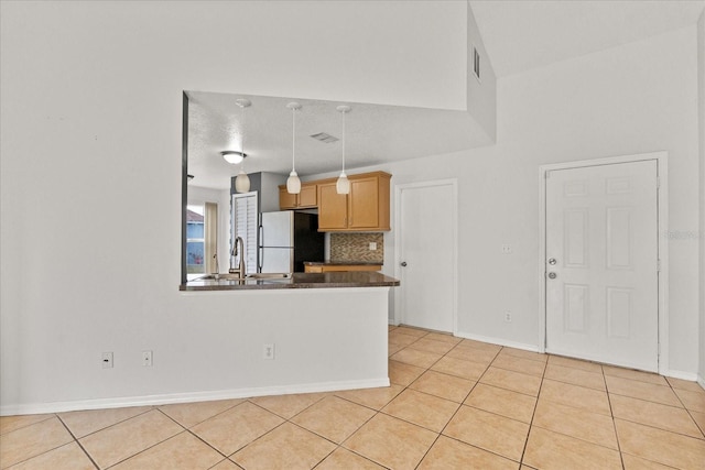 kitchen featuring dark countertops, light tile patterned floors, a sink, freestanding refrigerator, and a peninsula