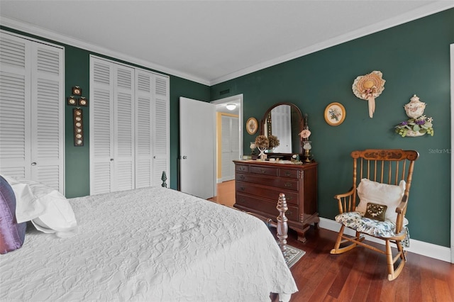 bedroom featuring ornamental molding, hardwood / wood-style floors, and two closets