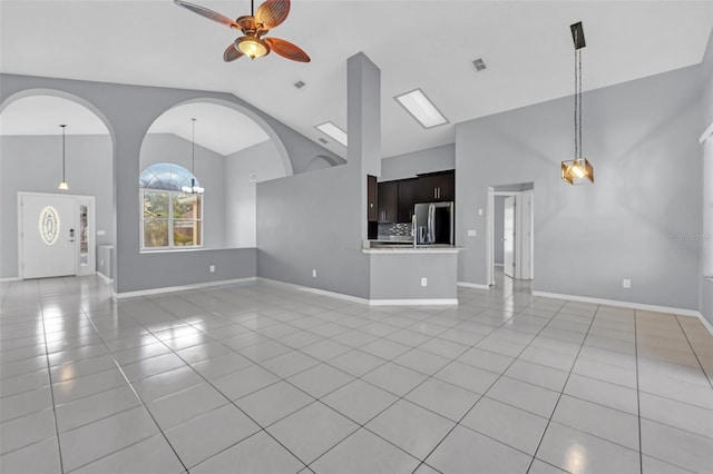 unfurnished living room with ceiling fan with notable chandelier, light tile patterned floors, and high vaulted ceiling