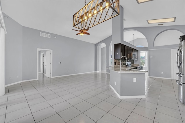 kitchen with light tile patterned flooring, light stone counters, vaulted ceiling, dark brown cabinets, and kitchen peninsula