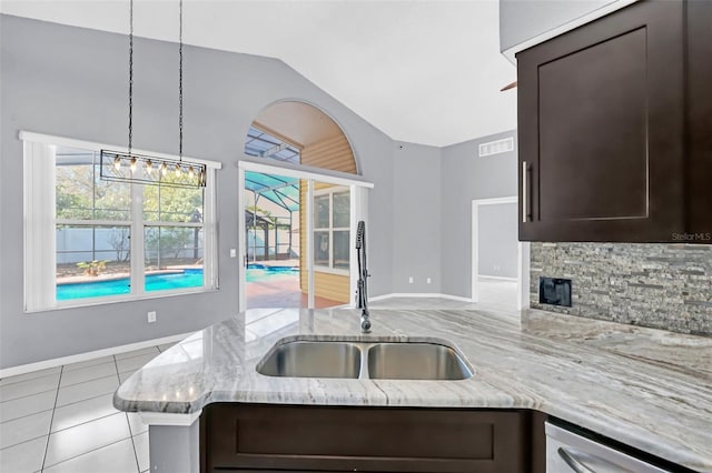 kitchen with light stone counters, vaulted ceiling, sink, and dark brown cabinets