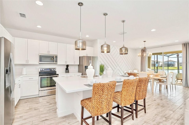 kitchen featuring a kitchen breakfast bar, a kitchen island, pendant lighting, stainless steel appliances, and white cabinets