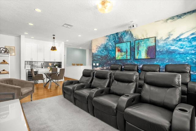 cinema featuring wine cooler, light hardwood / wood-style floors, and a textured ceiling