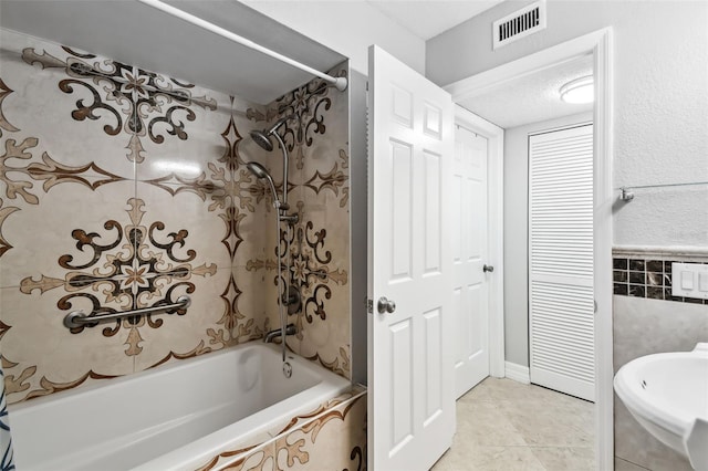 bathroom with tile patterned floors, tiled shower / bath combo, sink, and tile walls