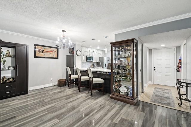 interior space featuring wood-type flooring, decorative light fixtures, a textured ceiling, ornamental molding, and appliances with stainless steel finishes