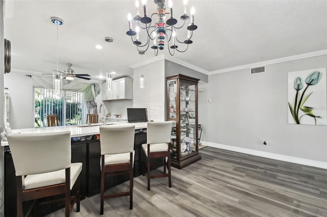 dining space with ornamental molding, wood-type flooring, ceiling fan with notable chandelier, and a textured ceiling