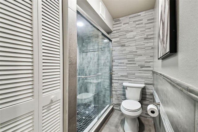 bathroom with a shower with shower door, tile walls, and toilet