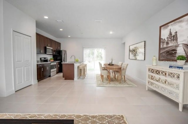 kitchen with a kitchen island with sink, dark brown cabinets, stainless steel appliances, and light tile patterned flooring