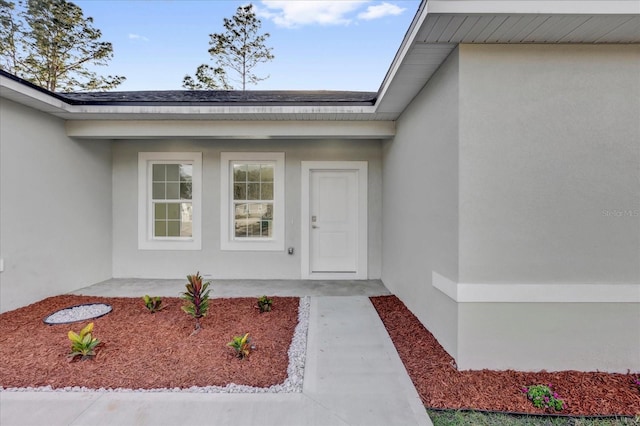 view of exterior entry featuring a shingled roof and stucco siding