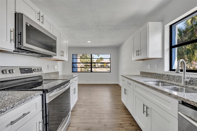 kitchen featuring sink, light wood-type flooring, stainless steel appliances, light stone countertops, and white cabinets