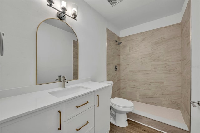 bathroom featuring vanity, hardwood / wood-style floors, toilet, and a tile shower