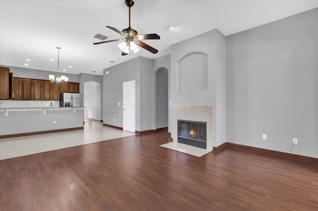 unfurnished living room featuring a tiled fireplace, ceiling fan with notable chandelier, and dark hardwood / wood-style flooring