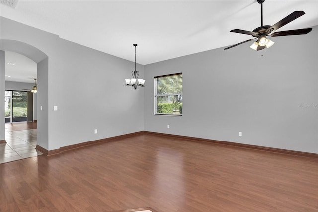 spare room featuring wood-type flooring, ceiling fan with notable chandelier, and a wealth of natural light