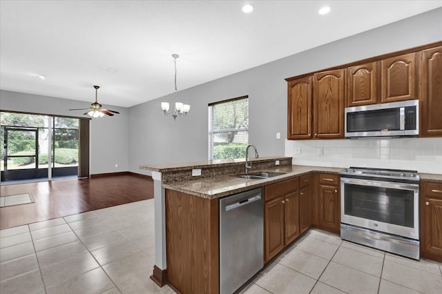 kitchen featuring sink, hanging light fixtures, appliances with stainless steel finishes, kitchen peninsula, and dark stone counters