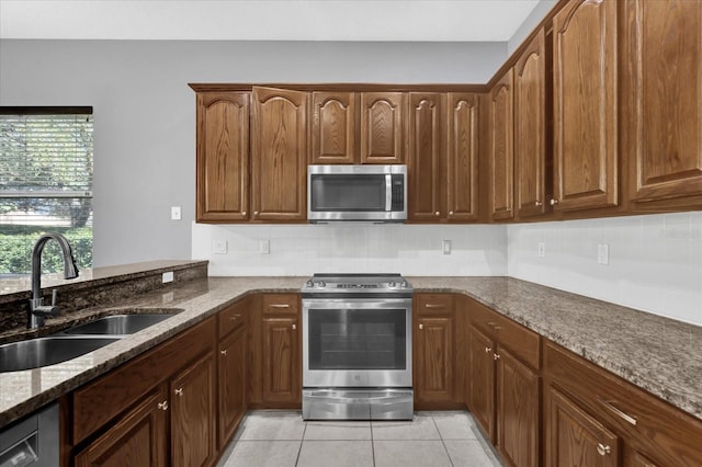 kitchen with sink, light tile patterned floors, stone counters, stainless steel appliances, and tasteful backsplash