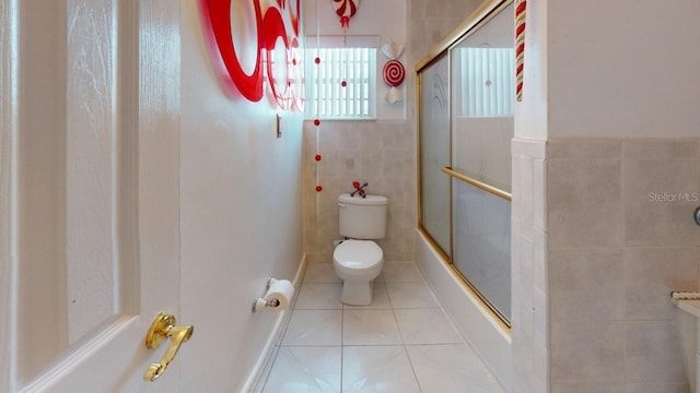 bathroom featuring tile walls, tile patterned flooring, toilet, and combined bath / shower with glass door