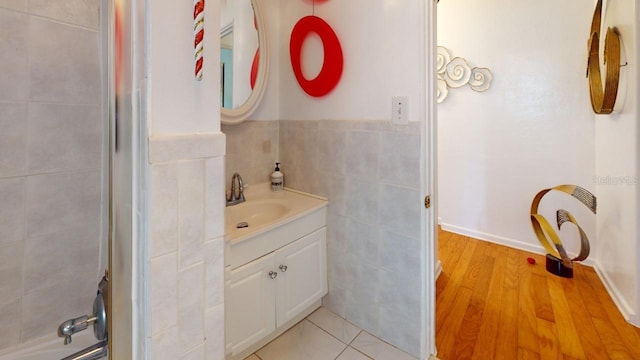 bathroom with tiled shower, vanity, hardwood / wood-style floors, and tile walls