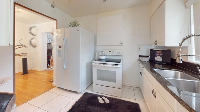 kitchen with sink, white appliances, white cabinets, light tile patterned flooring, and dark stone counters