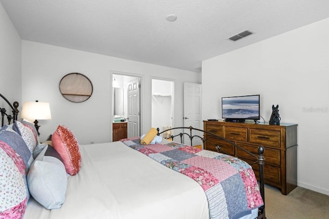 carpeted bedroom featuring ensuite bath and a textured ceiling