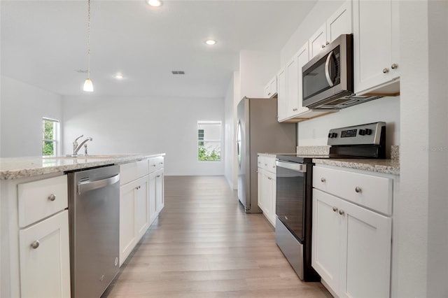 kitchen with decorative light fixtures, white cabinets, light stone counters, stainless steel appliances, and plenty of natural light