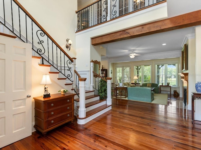 staircase with ceiling fan, a fireplace, wood finished floors, a towering ceiling, and crown molding