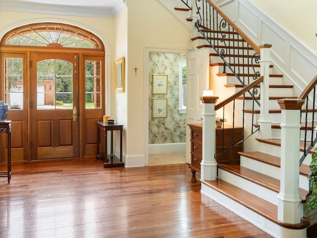 foyer entrance featuring baseboards, hardwood / wood-style floors, crown molding, and wallpapered walls