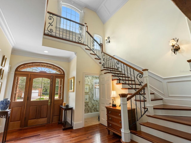 foyer entrance featuring a wainscoted wall, wood-type flooring, a decorative wall, a towering ceiling, and ornamental molding