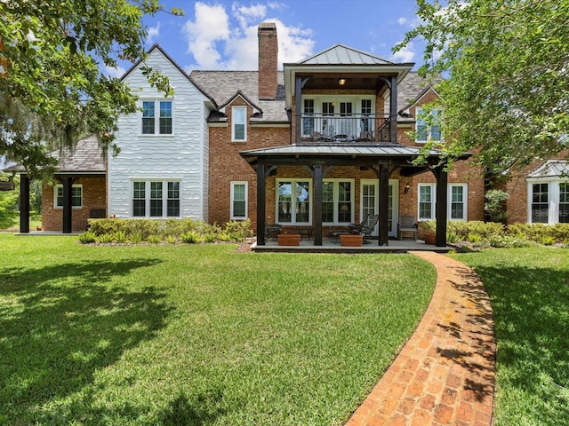 back of property featuring a balcony, a standing seam roof, a yard, and brick siding