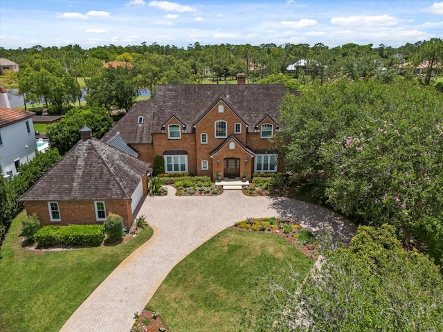 view of front of house featuring brick siding, decorative driveway, a chimney, and a front lawn