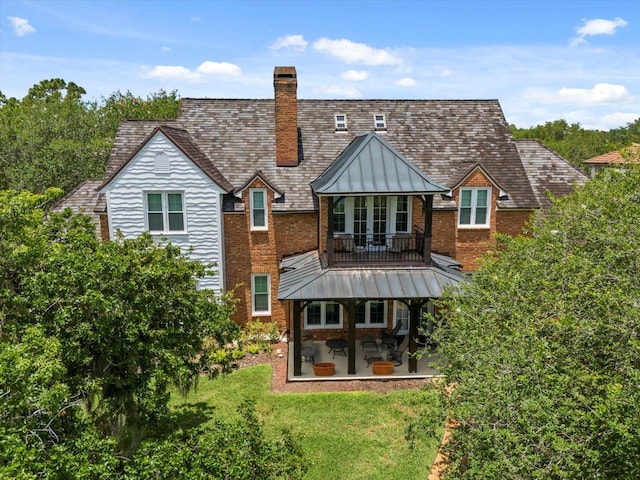 rear view of property with a standing seam roof, a patio, brick siding, a yard, and a chimney