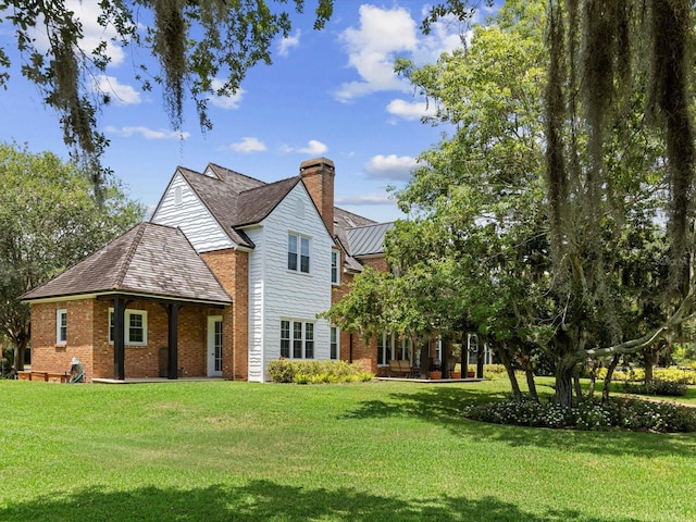 back of property with a chimney, metal roof, a standing seam roof, a yard, and brick siding