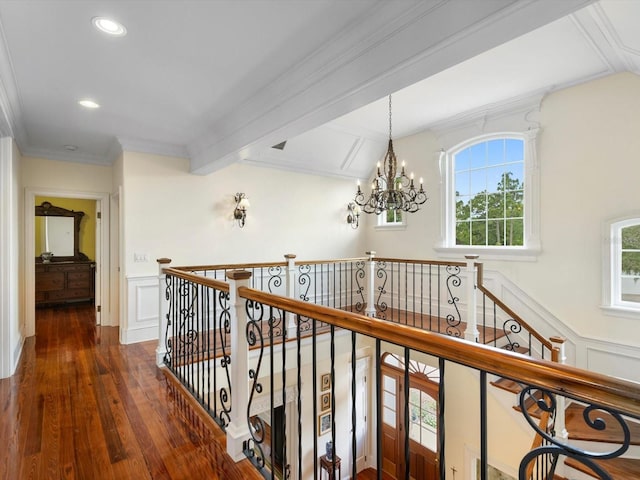 corridor with ornamental molding, a wainscoted wall, an inviting chandelier, and wood finished floors