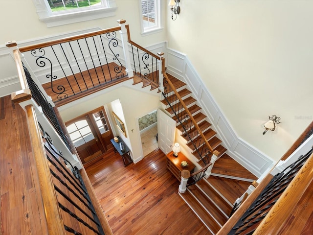 stairs featuring a wealth of natural light, wood-type flooring, a decorative wall, and a towering ceiling