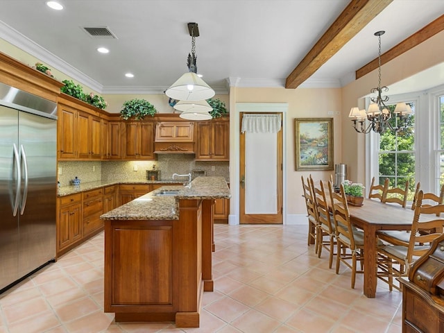 kitchen featuring visible vents, brown cabinetry, backsplash, a sink, and built in fridge