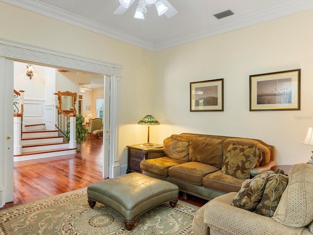 living area featuring ceiling fan, wood finished floors, visible vents, stairs, and ornamental molding