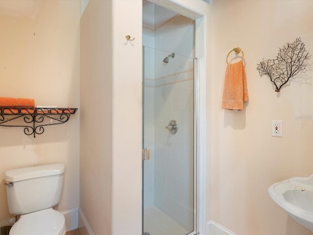 bathroom featuring toilet, a shower stall, and baseboards