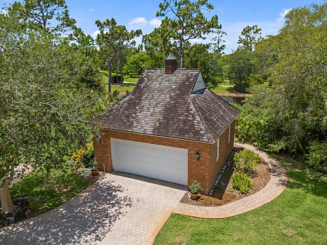 view of front of home featuring an attached garage, brick siding, decorative driveway, a chimney, and a front yard