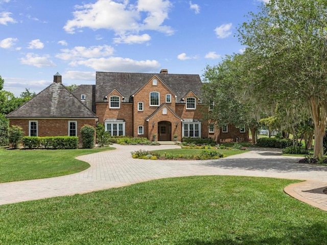 view of front of home with driveway, brick siding, a chimney, and a front yard