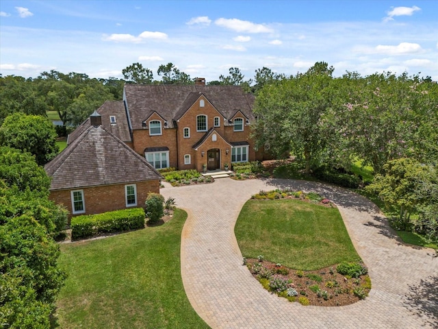 view of front facade featuring a chimney, brick siding, decorative driveway, and a front yard