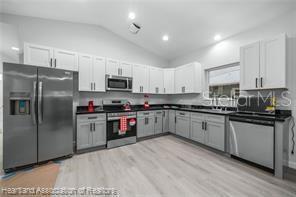 kitchen with light wood-type flooring, stainless steel appliances, vaulted ceiling, and white cabinets