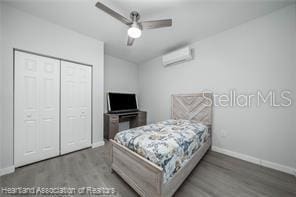 bedroom featuring hardwood / wood-style flooring, an AC wall unit, ceiling fan, and a closet