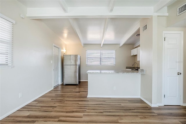 kitchen featuring visible vents, beamed ceiling, freestanding refrigerator, and white cabinetry