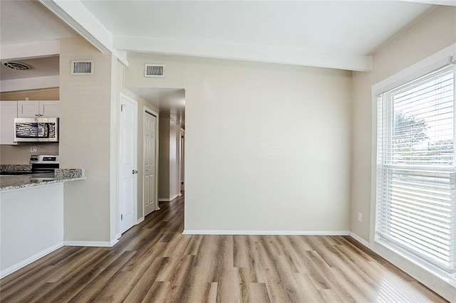 empty room featuring light wood finished floors, visible vents, and beamed ceiling